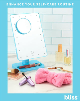 An LED Vanity Mirror (with Built-In Speaker & Hands-Free Calling), makeup products, a pink headband, and a purple facial roller are arranged on a countertop. Text at the top reads "Enhance your self-care routine" with "bliss" at the bottom right corner. The built-in speaker adds ambiance while bottles of perfume or skincare sit in the background.