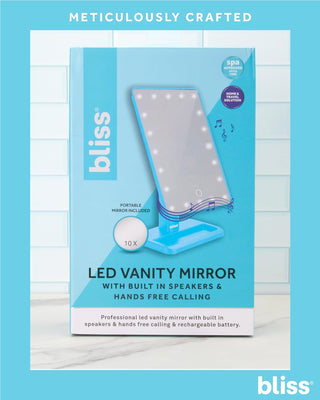 The image displays the product packaging for the "bliss LED Vanity Mirror (with Built-In Speaker & Hands-Free Calling)." The box highlights a portable mirror with built-in Bluetooth speakers and hands-free calling capability. Featuring 10x magnification, the predominantly blue and white packaging showcases its many labeled features.