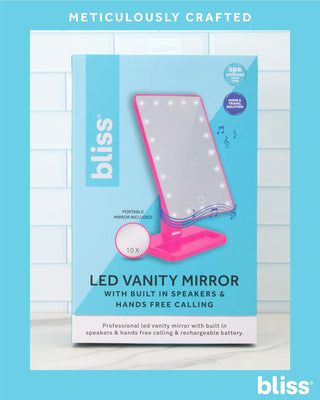 Image shows the packaging for a product called "LED Vanity Mirror (with Built-In Speaker & Hands-Free Calling)" by bliss, displayed against a light blue tiled background. The packaging highlights features including Bluetooth speakers, hands-free calling, 10x magnification, and a rechargeable battery.