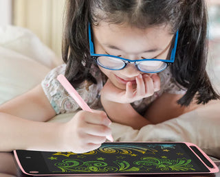 A young girl with glasses lies on a bed and uses a digital stylus to draw colorful designs on her 8.5" Multicolor LCD Drawing & Doodling Pad from Gabba Goods. The screen displays vibrant patterns, including stars and swirls. The girl appears focused and engaged in her creative activity.