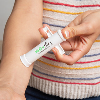 Close-up of a person using the Bug Bite Thing Insect Bite Relief & Sting Tool (2-Pack) on their forearm. The white suction tool is being applied to the skin to potentially provide insect bite relief. The person wears a multicolored striped sweater.