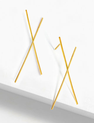 Sonia Hou Jewelry's Chopstick Earrings feature a minimalist design with two thin gold rods crossing diagonally, displayed on a white background. These earrings boast a sleek, modern aesthetic with geometric elements that subtly echo Asian culture.