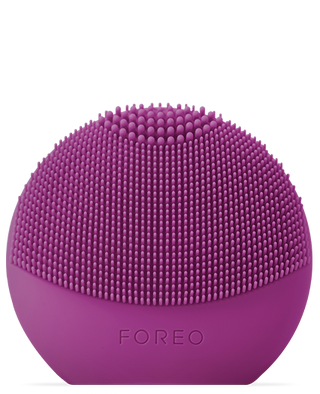 The LUNA "fofo" Smart Facial Cleansing Device by FOREO is a purple, round gadget with a textured surface covered in small silicone bristles. The bottom part features a smooth surface with the word "FOREO" imprinted on it. This device offers a personalized cleansing routine along with skin analysis for optimized skincare.