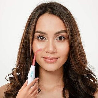 A woman with long, brown hair uses the bliss High Frequency Electrotherapy & Facial Wand (with Attachments Included) on her right cheek. She is smiling softly and has a clear complexion. The background is plain white, suggesting she might be enjoying the benefits of high frequency electrotherapy for acne treatment.