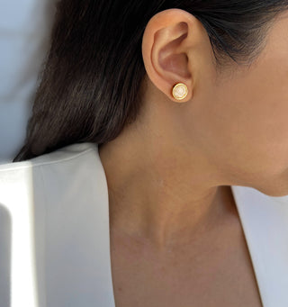 A close-up side view of a woman showcasing the exquisite Fire White Quartz 3-Way Earrings by Sonia Hou Jewelry. She is wearing a white blazer, and her dark hair cascades down gracefully, drawing attention to the shimmering earrings and part of her ear. The elegant background is softly blurred.