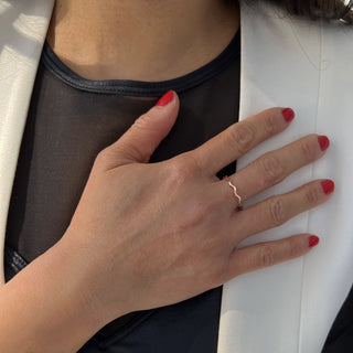 A person with red nail polish is wearing a black sheer top under a white blazer. They have placed their hand, adorned with the Noodle Ramen Ring from Sonia Hou Jewelry on their ring finger, on their chest. Sunlight casts a soft shadow on their hand and blazer, adding an air of timeless elegance reminiscent of Asian culture.