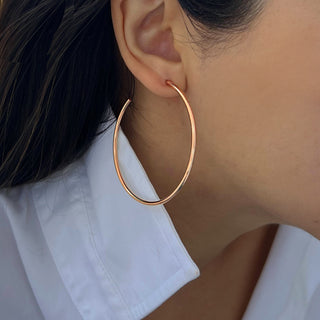 Close-up of a person wearing Perfect Hoop Earrings by Sonia Hou Jewelry, showcasing their smooth, metallic finish. The person has dark hair pulled back and is adorned with a white collared shirt, effortlessly highlighting the classic hoop design.