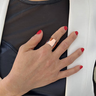 Close-up of a person's hand with red nail polish, adorned with the Rich Chunky Wide Cigar Band Ring by Sonia Hou Jewelry on the middle finger. The hand rests on their chest, which is covered by a black top and a white jacket, making a bold statement in this wardrobe essential ensemble.