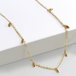 Experience the epitome of elegance with the Minimalist Rice Bead Chain Necklace from Sonia Hou Jewelry. This delicate gold necklace features a fine chain adorned with evenly spaced, teardrop-shaped pendants, symbolizing wealth and good health. Presented against a plain white background, it perfectly highlights its sophisticated design.