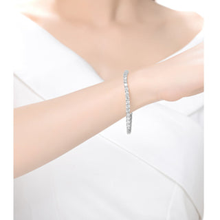 A person wearing a white, off-shoulder top showcases an elegant accessory: the Genevieve White Gold Plated Tennis Bracelet with Cubic Zirconia. The arm is gracefully positioned against a soft, white background, highlighting the bracelet's elegance.